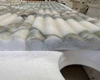 Könnte beinhalten: Eine rechteckige Platte aus weißem Marmor mit einer sich wiederholenden geriffelten oder gewellten Oberflächenstruktur. Der Stein zeigt durchgehend natürliche graue und beige Aderungen mit einer polierten Oberfläche auf den Kanten.