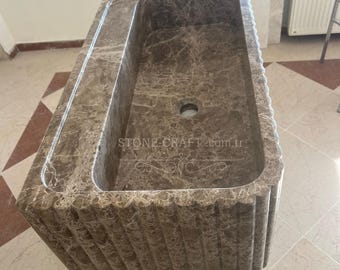 May include: A rectangular brown marble sink featuring a fluted exterior design with vertical grooves. The basin has a central drain hole and the text STONE-CRAFT.com.tr engraved on the interior floor along with a decorative scroll pattern.