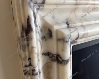 May include: A fireplace mantel crafted from white marble featuring prominent dark brown and grey veining. The structure displays a multi-layered, stepped profile with rounded edges and smooth surfaces, showcasing natural stone patterns throughout.