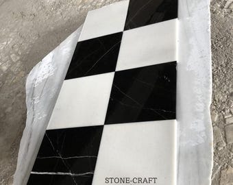 May include: A rectangular marble tile with a checkerboard pattern of black and white squares. The tile has a polished finish and the text "STONE-CRAFT" is visible. The tile is resting on a larger, rough-edged marble slab.