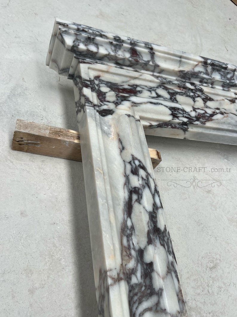 Puede incluir: Una repisa de chimenea de m&aacute;rmol blanco con vetas de color p&uacute;rpura oscuro, acabado pulido y bordes moldeados. La estructura de piedra muestra un patr&oacute;n de alto contraste con vetas violetas intensas sobre un fondo blanco. Texto: STONE-CRAFT.com.tr.