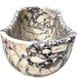 May include: A deep, oval-shaped bowl crafted from polished stone featuring a complex, high-contrast pattern of creamy white, beige, and dark charcoal gray veining throughout the entire exterior and interior surface of the vessel.