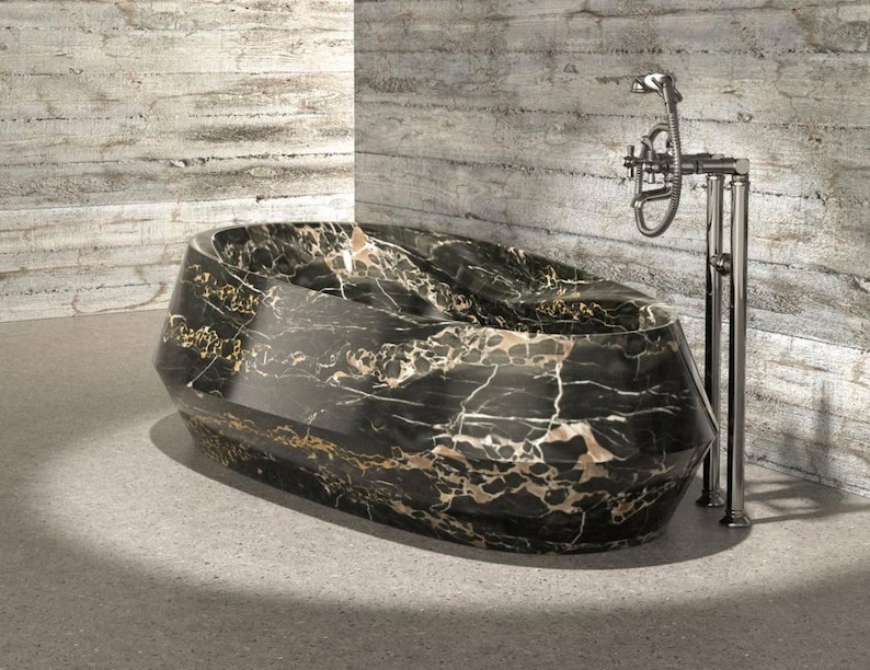 May include: A freestanding oval bathtub featuring a polished black marble finish with prominent white and gold veining. The tub has a faceted, geometric exterior design and is paired with a tall, chrome-finished floor-mounted faucet fixture.