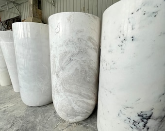 May include: A row of white marble planters with varying patterns and textures. The planters are cylindrical and have a smooth, polished finish.