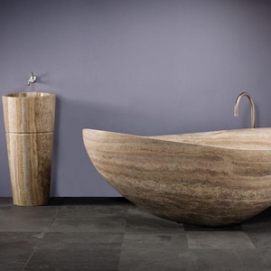 May include: A freestanding, oval-shaped bathtub and a matching cylindrical pedestal sink, both crafted from beige and brown veined natural stone. The bathtub features a curved, boat-like silhouette, and the sink includes a small metal faucet.