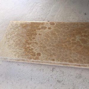 May include: A rectangular, light brown stone slab with a textured surface. The stone has a pattern of darker brown, irregular shapes across its surface. The edges of the slab are smooth and finished. The stone is likely for construction or design.