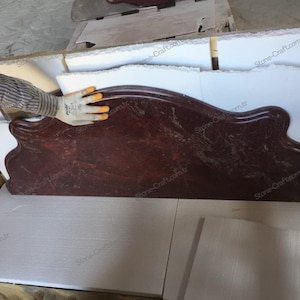 May include: A dark red, marble-like countertop with a unique, curved design. The countertop has a polished finish and a natural, veined pattern. The shape is reminiscent of a decorative shelf or a unique architectural element.
