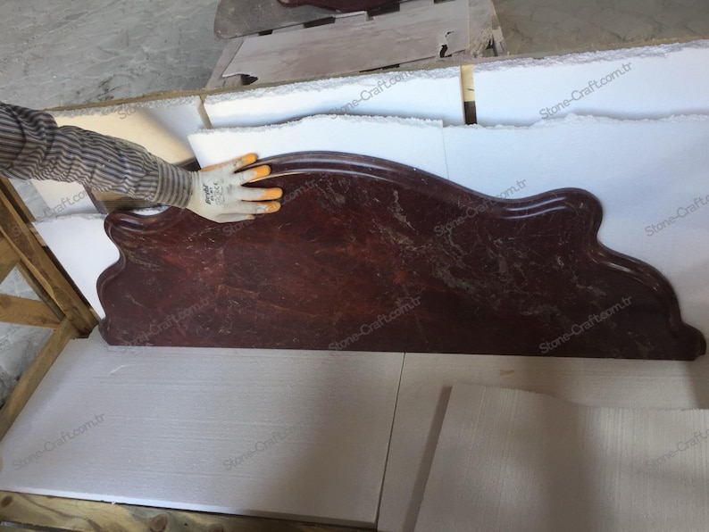 May include: A dark red, marble-like countertop with a unique, curved design. The countertop has a polished finish and a natural, veined pattern. The shape is reminiscent of a decorative shelf or a unique architectural element.