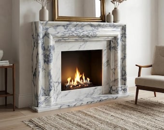May include: A fireplace mantel crafted from white marble with prominent blue-grey veining. The structure features a rectangular opening containing a burning fire. A tall, arched mirror with a gold frame is mounted directly above the mantelpiece.