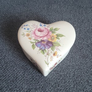 Pode incluir: Uma caixa de cerâmica branca em forma de coração com um design floral com flores rosa, amarelas e azuis.