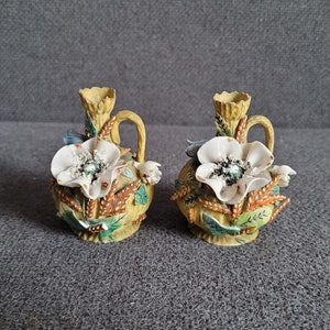 Peut inclure: Deux petits vases en céramique avec des motifs floraux. Les vases sont jaunes avec des fleurs blanches et des feuilles vertes.