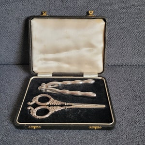 May include: A black velvet lined box with a silver nutcracker and a pair of silver scissors with ornate handles.