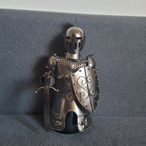 Ein moderner Flaschenständer aus Metall in Form eines Ritters mit Schild und Schwert, wobei der Ständer auf die Flasche gestellt wird