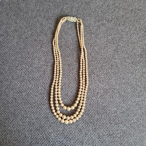 Peut inclure: Un collier de perles multi-rangs avec un fermoir argenté. Les perles sont de couleur crème et ont un léger lustre.