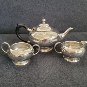 May include: A silver tea set with a teapot, creamer, and sugar bowl. The set has an ornate design with floral patterns.