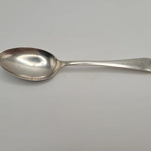 Peut inclure: Une cuillère en argent avec un bol arrondi et un long manche fin. La cuillère a une surface brillante et réfléchissante et un petit motif gravé au bout du manche. La cuillère est probablement destinée à manger ou à servir des aliments.