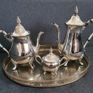 Può includere: Un set da tè in argento con una teiera, un creamer e una zuccheriera su un vassoio d'argento. Il set ha un design tradizionale con dettagli decorativi.