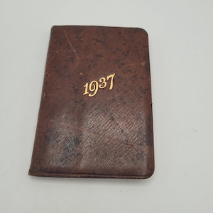 May include: A small, rectangular, brown leather-bound book with the gold-colored year "1937" embossed on the cover. The leather has a textured appearance and shows signs of wear.