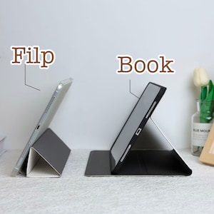 May include: Two tablet cases, one in black and one in gray, are shown in a side-by-side comparison. The case on the left is in the "Flip" position, while the case on the right is in the "Book" position.