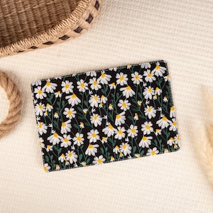 May include: A black clutch with a white daisy floral pattern embroidered on the front.