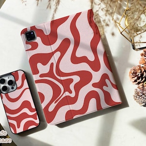 May include: A smartphone case and a tablet cover featuring a matching wavy, abstract pattern in shades of red and light pink. The phone case has a cutout for a camera array, and the tablet cover is a folio style with a visible camera cutout.