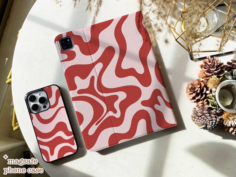 May include: A smartphone case and a tablet cover featuring a matching wavy, abstract pattern in shades of red and light pink. The phone case has a cutout for a camera array, and the tablet cover is a folio style with a visible camera cutout.
