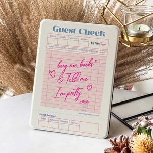 Puede incluir: Un bloc de notas de cheque de huésped blanco con corazones rosas y el texto "buy me books & tell me I'm pretty xoxo". El bloc de notas tiene una sección para la fecha, la mesa, los invitados, el servidor y una sección de recibo con la fecha, el monto, los invitados y el servidor.