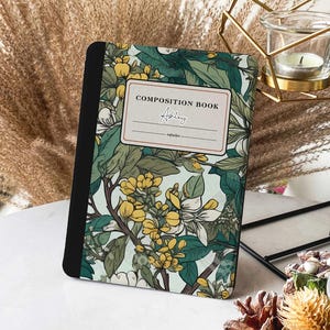 Può includere: Un quaderno di composizione con un design floreale con fiori gialli e bianchi su uno sfondo blu chiaro. Il quaderno ha una rilegatura nera e il testo "COMPOSITION BOOK" e il nome "Adley" sono stampati sulla copertina.