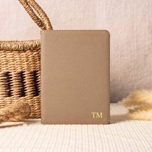 May include: A light brown leather notebook with the initials "TM" embossed in gold on the front cover.