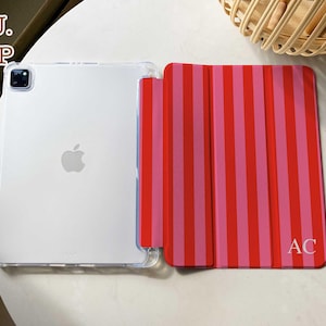 May include: A tablet case featuring a clear back and a folding front cover with vertical red and pink stripes. The front cover displays the letters AC in the bottom right corner. The text TPU. FILP is visible in the upper left corner of the image.