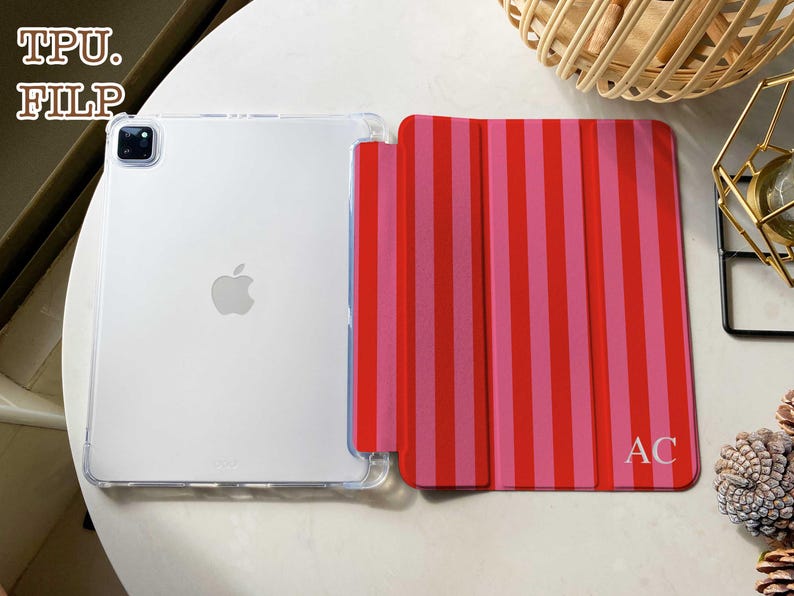 May include: A tablet case featuring a clear back and a folding front cover with vertical red and pink stripes. The front cover displays the letters AC in the bottom right corner. The text TPU. FILP is visible in the upper left corner of the image.