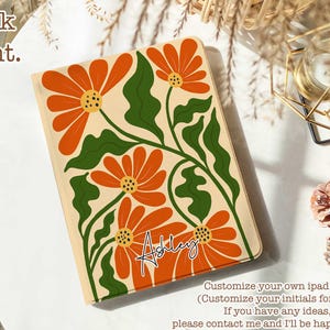 Puede incluir: Una funda para iPad de color crema con un diseño floral con flores naranjas y verdes. El texto "Ashley" está escrito en cursiva negra en la funda.