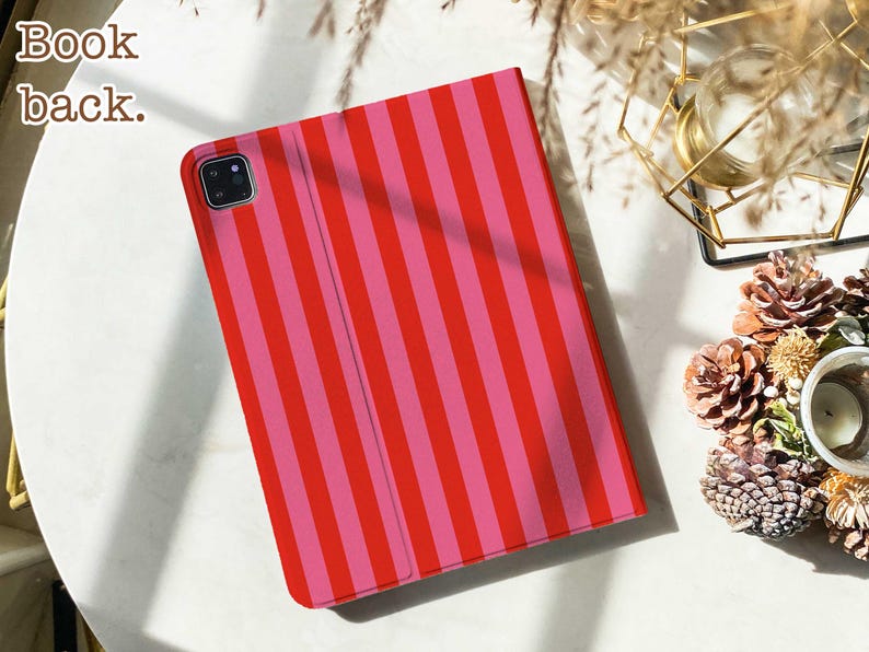 May include: A rectangular tablet case featuring a vertical striped pattern in alternating shades of bright red and pink. The case includes a square camera cutout in the upper left corner and the text Book back. printed in the upper left corner area.