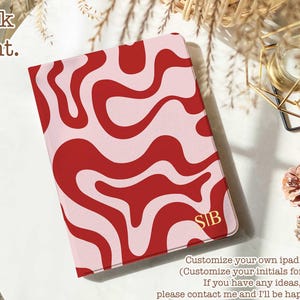 Może przedstawiać: Etui na iPada z czerwonym i jasnoróżowym falistym wzorem. Inicjały "SIB" są złote w prawym dolnym rogu. Tekst "Book front" znajduje się w lewym górnym rogu.
