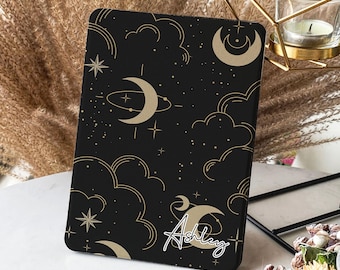 May include: Black and gold tablet case with a celestial pattern of moons, stars, and clouds. The name "Ashley" is written in gold script on the bottom right corner.