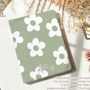 May include: A sage green iPad case with a white daisy pattern and the name "Ashley" written in black cursive. The text "Customize your own ipad case (Customize your initials for free) If you have any ideas, please contact me and I'll be happy to help!" is written below the case.