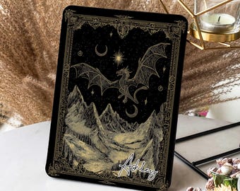 May include: Black rectangular tablet case featuring a gold dragon and mountain design. The dragon flies over mountains under a night sky with a moon and stars. The name "Ashley" is written in cursive.