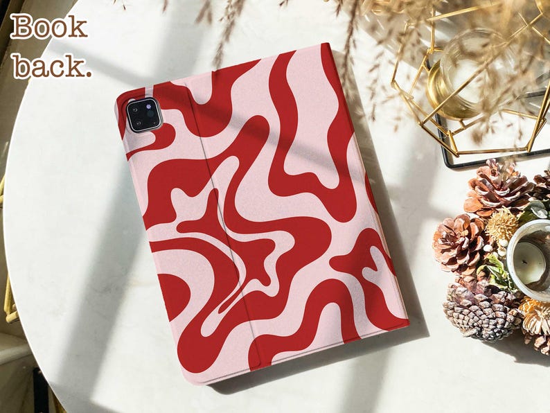 May include: A tablet case featuring a wavy, abstract pattern in bold red and light pink. The case has a rectangular shape with a dedicated cutout for a camera lens in the top left corner. The text "Book back." is printed in the top left corner.