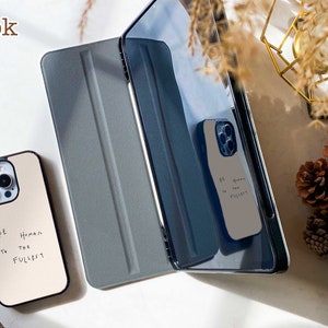May include: Two phone cases with a white background and black text that reads "Be Human to the fullest". The cases are on a white surface with a gray and black tablet case.