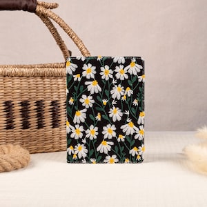 May include: A black passport holder with a white daisy floral pattern. The holder is made of fabric and has a subtle sheen.