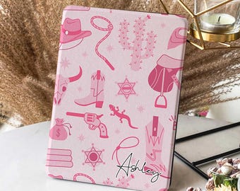 May include: Pink and white e-reader case with a western theme. The case features a repeating pattern of pink cowboy boots, cacti, stars, and other western icons. The name "Ashley" is written in cursive at the bottom of the case.
