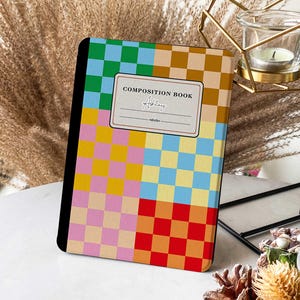 May include: A composition book with a checkered pattern in shades of green, blue, yellow, pink, orange, and red. The book has a label that says "Composition Book" and a blank space for a name. The name "Addley" is written in cursive in the blank space.