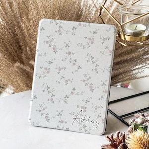 Pode incluir: Uma capa branca com padrão floral para um leitor de e-books com o nome "Ashley" escrito em itálico preto no canto inferior direito.