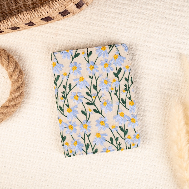 May include: A small, rectangular, cream-colored linen pouch with a floral pattern. The pouch is embroidered with blue and yellow flowers.
