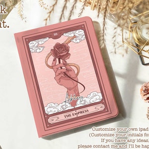 Puede incluir: Una funda rosa para iPad con una mano sosteniendo una rosa y las palabras "The Empress" en la parte delantera. La funda es personalizable con iniciales.