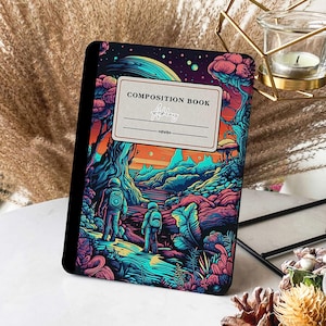 May include: A composition book with a colourful illustration of astronauts exploring a fantastical landscape. The cover features a vibrant sunset, lush greenery, and a swirling galaxy. The title "COMPOSITION BOOK" is printed in white on a beige rectangle, with the name "Ashley" handwritten below it.