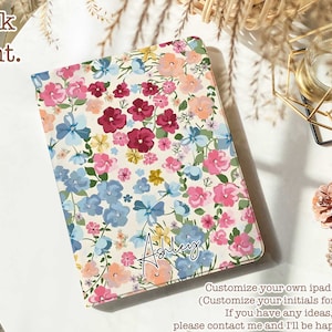 May include: A white iPad case with a floral pattern in shades of pink, blue, and yellow. The name "Ashley" is written in cursive on the case.