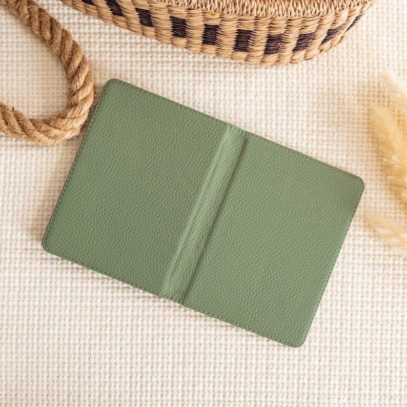 May include: A closed green leather journal with a textured cover. The journal is lying on a white textured surface.