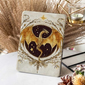 Peut inclure: Un dragon doré aux ailes déployées est représenté sur un fond bleu foncé avec des étoiles dorées. Le dragon est entouré d'une couronne dorée avec une étoile au sommet. Le motif est sur un fond blanc avec une surface texturée.