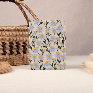 May include: A light blue and yellow floral embroidered fabric clutch with a simple design.